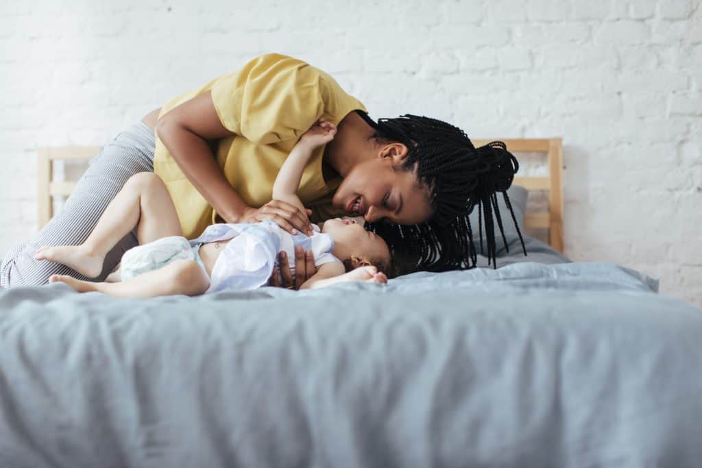 Beautiful African woman cuddling her baby daughter in bedroom.
